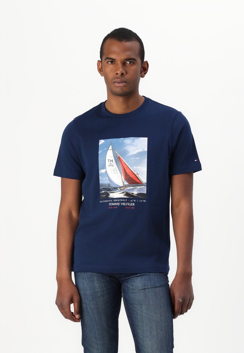 Mørkeblå bomulls t-skjorte med et seilbåtmotiv i sentrum, med røde og hvite seil, og "Tommy Hilfiger"-tekst under.
