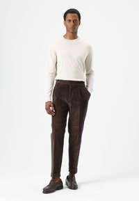 Pantalon en velours côtelé marron à coupe droite, doté de poches latérales et d'une longueur légèrement raccourcie, associé à une chemise crème à manches longues.