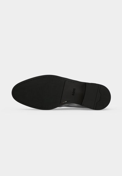 Semelle de chaussure habillée en cuir noir avec le nom de la marque "BOSS" visible près du centre.