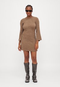 Robe en tricot côtelé marron à manches longues et silhouette ajustée. Assortie à des bottes grises jusqu'aux genoux, dotées de boucles et d'une texture brillante.