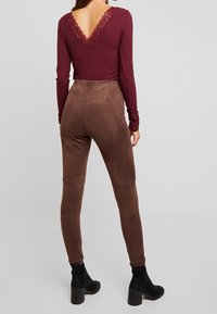 Haut bordeaux à manches longues avec col en V en dentelle, associé à un pantalon marron en suédine synthétique. Des bottines noires à talons complètent la tenue.