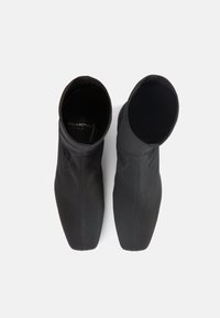 Μαύρα μποτάκια αστραγάλου με λείο, υφασμένο φινίρισμα. Διαθέτουν κλειστή μύτη και κομψή σιλουέτα. Το εσωτερικό είναι απαλό, χωρίς ορατά μεταλλικά στοιχεία.