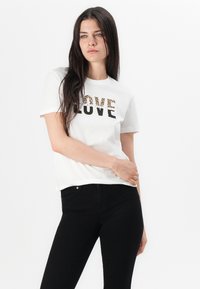 T-shirt en coton blanc avec des lettres noires et imprimé léopard épelant "LOVE". Assorti à un jean noir ajusté, présentant un look décontracté.