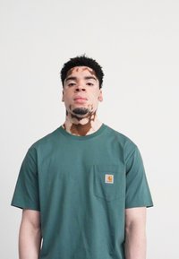 Green cotton t-shirt with short sleeves, round neckline, and chest pocket. Features a small embroidered logo on the pocket.