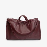 Sac à main en cuir rouge foncé avec une fermeture à cordon, une seule poignée et une longue bandoulière sur un fond blanc.