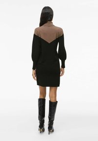Robe noire avec un accent en V marron à l'arrière supérieur, dotée de longues manches bouffantes et d'un col ; portée avec des bottes noires jusqu'aux genoux.