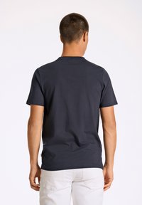 Tummansininen puuvillainen t-paita, jossa on lyhyet hihat, pyöreä kaula-aukko ja sileä pinta, esitetty takaviistosta. Ei näkyviä logoja tai graafisia kuvastoja.