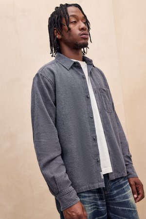 Chemise décontractée à manches longues en motif vichy bleu marine et blanc, dotée d'une fermeture à boutons sur le devant, d'un col et d'une poche poitrine. Portée par-dessus un t-shirt blanc.
