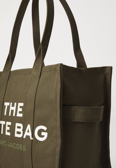Oliwkowa torba z płótna z podwójnymi uchwytami, z napisem "THE TOTE BAG" w białym kolorze. Zawiera boczną kieszeń i mocne szwy.