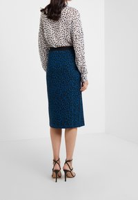 Leopard print skirt in teal with a fitted shape, paired with a sheer, patterned blouse featuring black and beige accents. Black strappy heels.