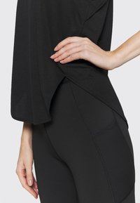 Černý atletický top s volnějším střihem a texturovanou látkou, kombinovaný s černými legínami s vysokým pasem, které mají švové detaily a boční kapsy.