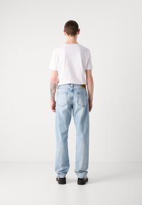 Vaqueros de mezclilla de un azul claro con un corte relajado, cinco bolsillos y una etiqueta de cuero marrón en la parte posterior, combinados con una camiseta blanca básica.