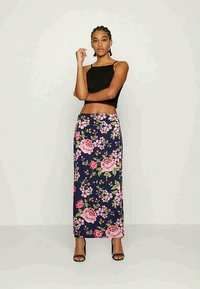 Saia maxi floral com fundo azul-marinho, apresentando rosas cor-de-rosa e folhas verdes. Usada com um top cropped preto e sapatos de salto abertos pretos.