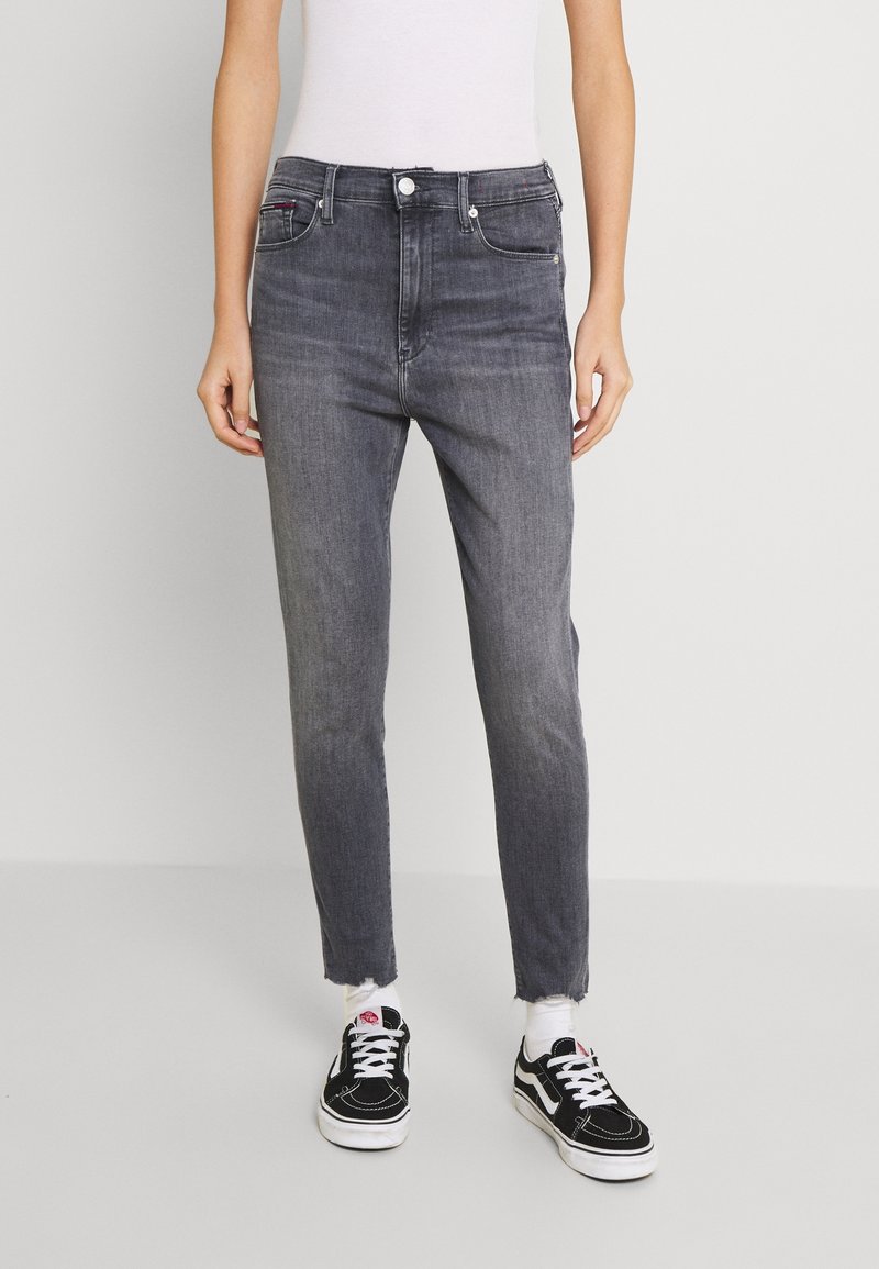 Graue High-Waist-Jeans mit schlanker Passform, mit ausgefranstem Saum, Fronttaschen und Knopfverschluss, kombiniert mit schwarzen Sneakers.