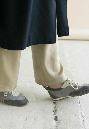 Zapatos grises y beige con materiales de gamuza y cuero; cuentan con cordones, texturas contrastantes y un acento verde en el talón.