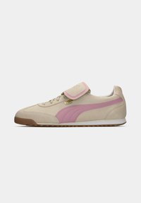 Beige semsket sneaker med rosa detaljer og borrelåsrem. Har en teksturert gummisåle og PUMA-merke i gull.