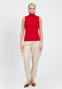 Rød ærmeløs turtleneck top, tætsiddende design, parret med beige cargo bukser med lynlås-lommer og opkrøllede ben; model i brune hæle.
