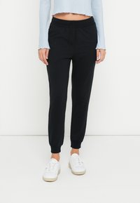 Zwarte joggerbroek met elastische tailleband en boorden, gemaakt van zachte stof. Gecombineerd met witte sneakers en een lichtblauw cropped topje.