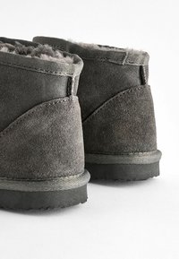 Grå mocka ankelstövlar med mjukt foder i pälsg material, platta gummisålar, förstärkt sömnad och en distinkt böjd design på sidorna.