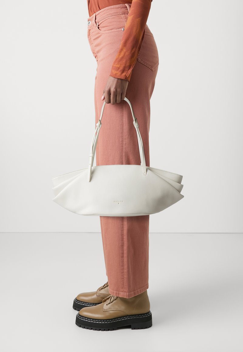 Sac à main en cuir blanc avec un design plié élégant et deux poignées. Associé à un pantalon rose clair et des bottes lacées beige.