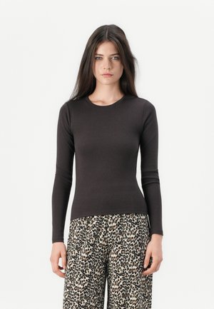 Schwarzes Langarmshirt aus weichem Stoff, eng anliegendes Design. Kombiniert mit weit geschnittenen Leopard-Print-Hosen in einem creme- und braunfarbenen Muster.