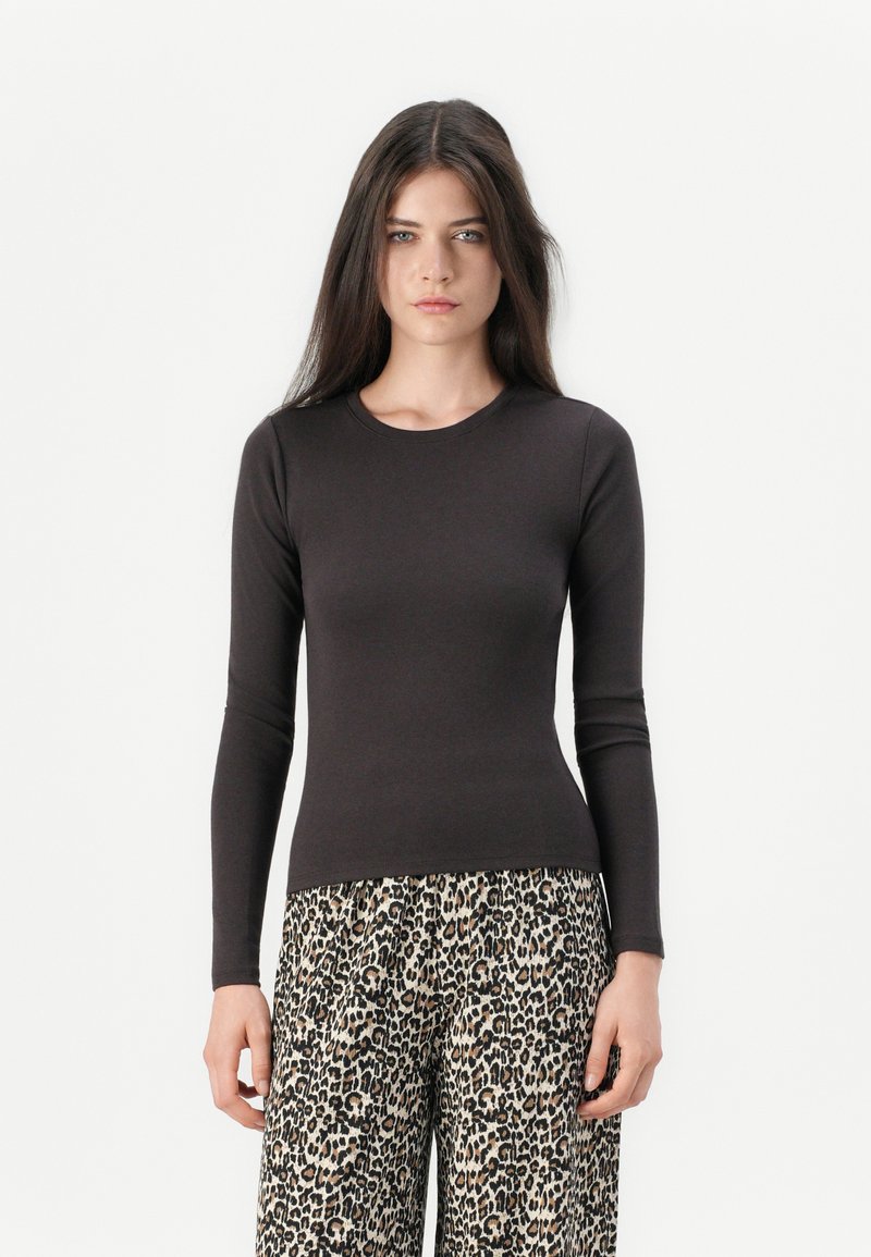 Schwarzes Langarmshirt aus weichem Stoff, eng anliegendes Design. Kombiniert mit weit geschnittenen Leopard-Print-Hosen in einem creme- und braunfarbenen Muster.