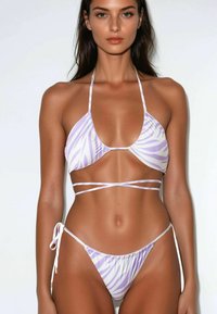 Set di bikini in stampa zebra viola e bianca. Il top ha una forma triangolare con spalline sottili, mentre il fondo presenta un taglio a vita bassa con lacci.