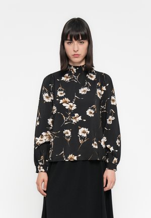 Blouse noire à manches longues avec imprimé floral en crème et beige, présentant un col haut et des détails froncés aux épaules et aux poignets.