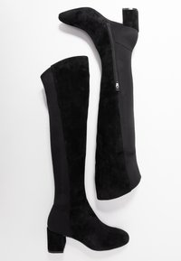 Botas negras hasta la rodilla hechas de ante y tela, con punta redonda, tacón cuadrado y detalle de cremallera lateral.