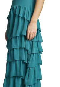 Abito teal con volants a strati in un tessuto testurizzato, dal design organico e fluido, con un primo piano dei dettagli arricciati.