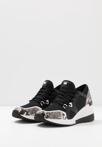 Zapatillas en blanco y negro con un diseño de estampado de serpiente en la puntera, tela de malla, cordones resistentes y una suela de goma texturizada.