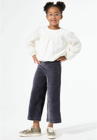 Witte blouse met lange mouwen en pofmouwen, gecombineerd met donkergrijze corduroy wijde broek en sneakers met luipaardprint.