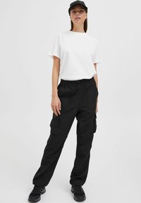 T-shirt bianco a collo rotondo abbinato a pantaloni cargo neri con vita elastica, numerose tasche e sneaker nere.