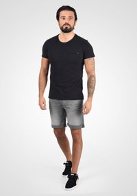 Melna T-kreka ar krūšu kabatu, apvienota ar gaiši pelēkiem denim šortiem ar sarullētām malām un melniem sporta apaviem ar zelta akcentiem.
