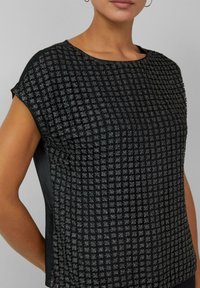 Czarny top o wzorzystej fakturze z motywem kratki, krótkimi rękawami oraz gładkim bocznym panelem dla kontrastu.
