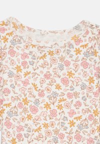 Floral-patterned cotton fabric featuring pink, blue, and yellow flowers on a white background; soft texture, rounded neckline, and short sleeves.