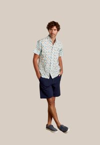Korte mouwen shirt met een lichtblauwe achtergrond en kleurrijke abstracte patronen; gecombineerd met marineblauwe shorts en grijze schoenen.
