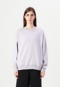 Ljuslila sweatshirt i mjukt tyg, med rund hals, långa ärmar och ribbade mudd. Matchad med svarta löst sittande byxor.