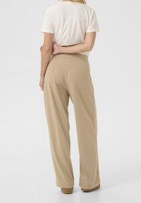 Béžové halenky s vysokým pasem a širokými nohavicemi, s hladkým povrchem a čistými liniemi. V kombinaci s bílým topem s krátkým rukávem.