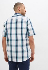 Camicia a maniche corte con bottoni di colore bianco con motivo a quadri blu e grigio, dotata di colletto e orlo curvo sul retro.