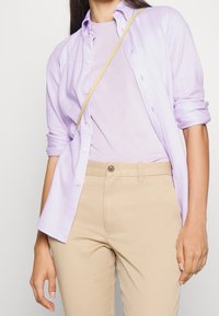 Camisa de botones de color púrpura claro sobre una camiseta púrpura clara, combinada con pantalones beige. La camisa tiene las mangas arremangadas y botones.