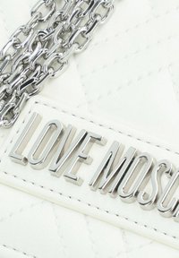 Borsa a tracolla bianca trapuntata con catena argentata e una placca argento ben visibile con il testo "LOVE MOSCHINO."