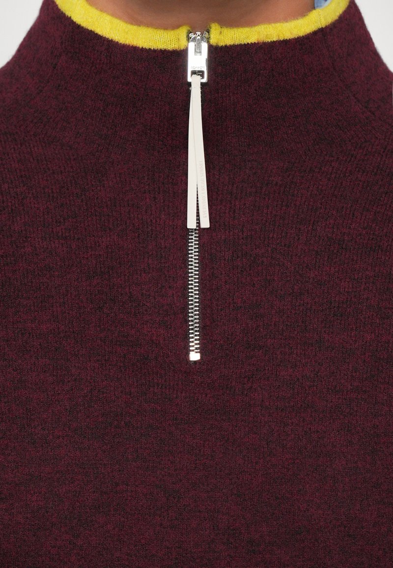 Bordeaux trui met gele kraag en zilveren rits. Zachte textuur, hoog gekleed ontwerp en ritsopening voor aanpasbaarheid.