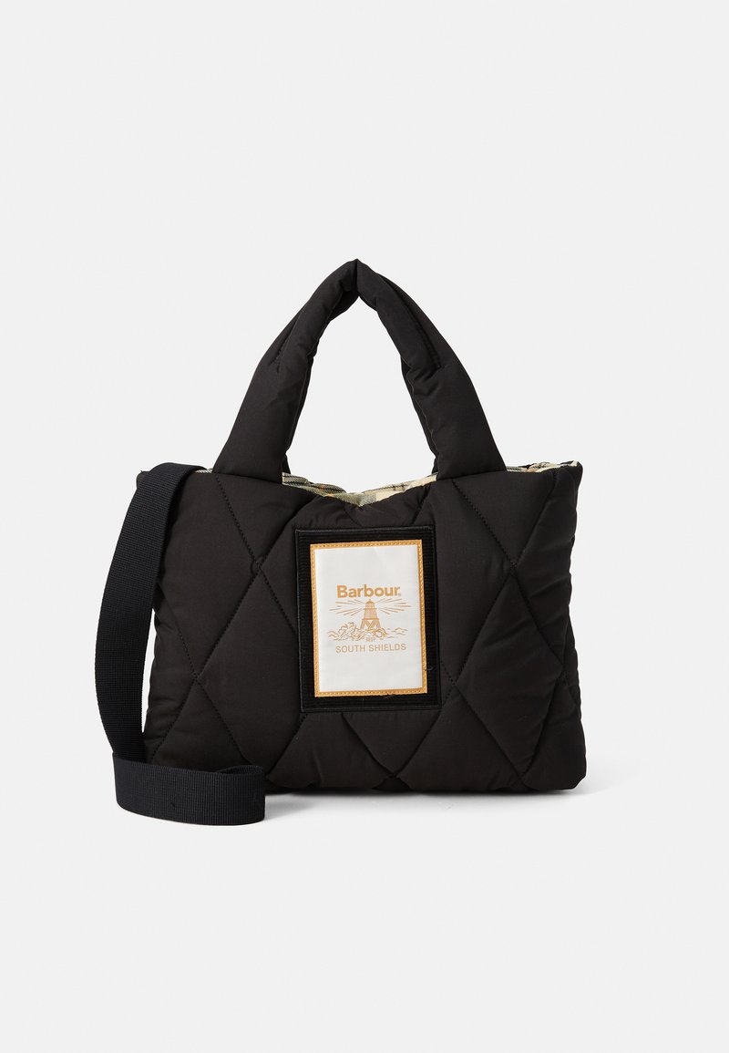 Czarna torba na ramię z pikowanej tkaniny, z wyściełanymi uchwytami, odpinanym paskiem na ramię oraz przednią etykietą z napisem "Barbour South Shields" i logo latarni morskiej.