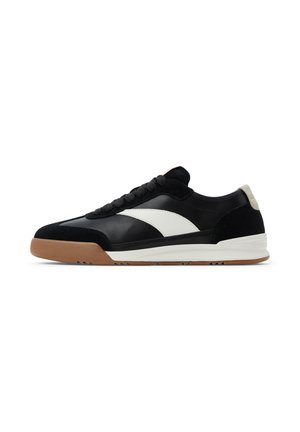Zapatilla de cuero en blanco y negro con acentos de ante, parte superior texturizada en negro, detalle de logo en blanco y suela de goma. Diseño de perfil bajo.