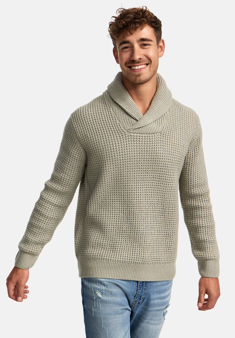 Light green knitted sweater with a wide shawl collar, textured pattern, and ribbed cuffs and hem. Worn with blue distressed jeans.