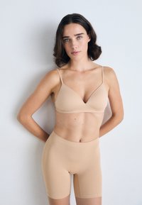 Lichtbeige bralette met verstelbare bandjes en een diepe V-hals, gecombineerd met bijpassende high-waisted boyshorts. Gladde, rekbare stof.