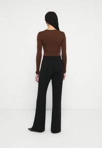 Hnedý rebrovaný top s dlhým rukávom v kombinácii s čiernymi širokými nohavicami s vysokým pásom, ktoré majú hladkú textúru a jemné švové detaily.