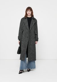 Manteau en laine mélangée vichy avec des revers surdimensionnés, motif noir et blanc, ouvert à l'avant, porté sur un pull noir et un pantalon large.