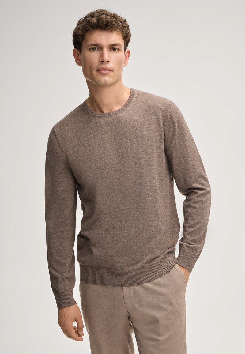 Brauner Strickpullover, Rundhalsausschnitt, lange Ärmel, gerippte Bündchen und Saum, weiche Textur, getragen mit hellbeigen Hosen. Keine sichtbaren Muster oder Logos.